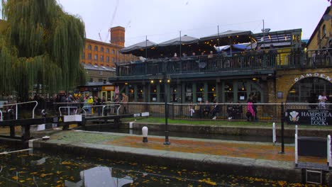 Pan-shot-across-famous-Camden-lock-area-and-market-with-shoppers-walking-by-in-north-London,-UK-on-a-cloudy-day
