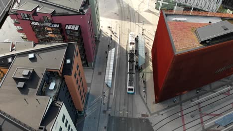 Public-tramway-stopping-at-station-near-downtown-buildings-in-Gothenburg,-aerial-view
