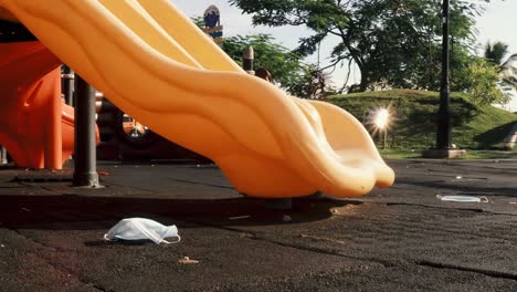 Eine-Dolly-Aufnahme-Einer-Orangefarbenen-Kinderrutsche-Aus-Plastik-Auf-Einem-Verlassenen-öffentlichen-Spielplatz,-Chirurgische-Gesichtsmasken-Lagen-Im-Park-Verstreut