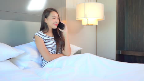 Young-Asian-woman-talking-on-a-mobile-phone-while-lying-on-a-bed-before-sleeping
