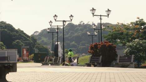 A-female-public-worker-of-the-Sanitations-Authority-of-Panama-City,-preoccupied-while-tying-a-knot-in-a-plastic-bag-of-the-trash-bin-she-has-just-emptied-in-a-park,-Causeway-of-Amador,-Panama-City