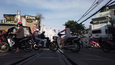 Tráfico-De-Motocicletas-Y-Peatones-Sobre-Vías-De-Tren-En-Un-Paso-A-Nivel-En-Saigón-En-Una-Soleada-Mañana-Clara-Desde-Un-ángulo-Bajo