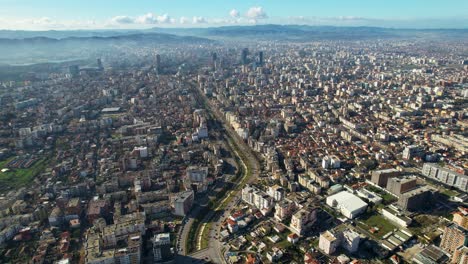Center-with-high-buildings-and-the-outskirts-of-the-capital-connected-by-river-of-Lana-in-Tirana,-Albania