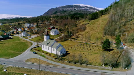 Aerial-drone-shot-of-Gimsoy-church-and-cemetery-in-Lofoten-Islands-surrounded-by-road-networ-in-Norway-at-daytime