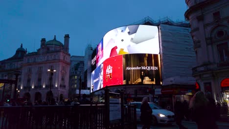 Pedestrians-illuminated-by-bright-advertising-screens-at-Picadilly-Circus,-Westminster,-London,-UK