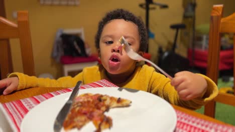 Cute-and-very-expressive-two-year-old-black-baby-eats-pizza-by-himself-with-a-fork-at-home