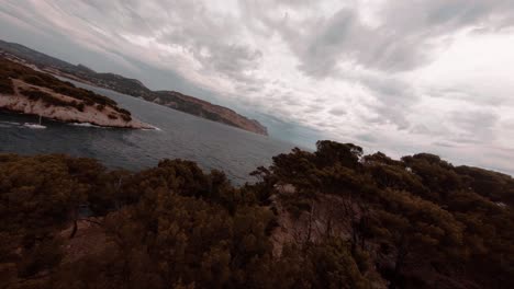 FPV-aeriel-view-over-the-mediterranean-sea-while-a-sail-boat-is-motoring-further-along-the-coastline-close-up