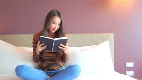 Close-up-of-a-young,-attractive-woman-sitting-cross-legged-on-a-bed-as-she-reads-through-a-book