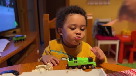 Impatient-two-year-old-black-baby-eats-pizza-at-home-fed-by-mum-wth-a-fork