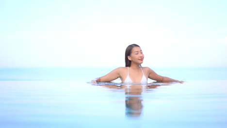 Attractive-Exotic-Woman-in-Infinity-Pool-With-Tropical-Skyline-Merges-With-Water-Surface,-Full-Frame