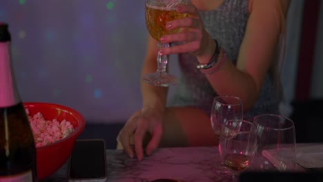 Beautiful-blonde-caucasian-white-girl-women-in-front-of-led-light-wall-in-a-dark-night-club-scene-neck-down-shot-as-she-drinks-from-champagne-wine-glass-and-popcorn-as-lights-flash-at-night-club