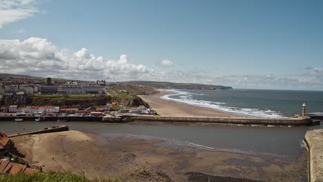 Town-of-Whitby-showing-harbour-entrance,-coastline-and-sandy-beach,-bright-sunny-day-North-Yorkshire-UK-England
