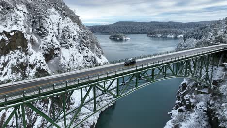 Umlaufende-Ansicht-Eines-Einsamen-Geländewagens,-Der-über-Eine-Brücke-Fährt,-Während-Schnee-Das-Umliegende-Land-Bedeckt