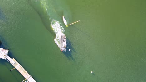 Aerial-top-down-of-wrecking-tug,-towing-and-dragging-submerged-sailboat-towards-the-dock