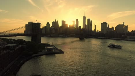 Brooklyn-Bridge-over-Hudson-River-and-golden-sunset-behind-Manhattan-skyline,-New-York