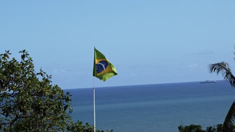 Brazil-flag-close-up-waving-in-the-wind-in-120fps-slow-motion-with-the-vast-ocean-in-the-background-in-the-historic-city-of-Olinda-in-Pernambuco,-Brazil