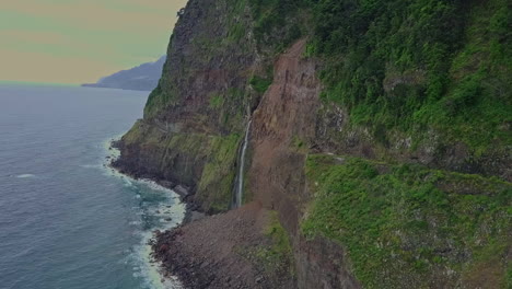 Orbiting-aerial-of-serene-waterfall-flowing-into-ocean-from-mountains,-Madeira