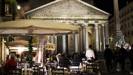 Outdoor-dining-at-a-restaurant-in-Rome,-Italy-at-night-outside-the-Pantheon-with-people-walking-by