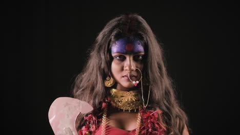 Live-Indian-Goddess-Kali-opens-her-eyes-and-looks-at-camera,-Indian-goddess-cosplay-with-long-hair-and-dark-background-in-studio