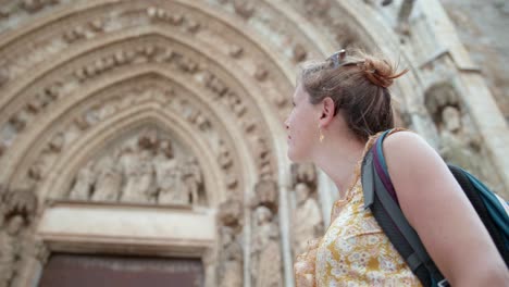 Woman-Traveler-Looking-And-Appreciating-The-Beautiful-Exterior-Of-Basílica-de-Santa-Maria-in-the-municipality-of-Castelló-d'Empúries,-Spain---low-angle-shot