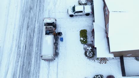 Aerial-view-of-a-dump-truck-picking-up-trash-on-a-snowy-day