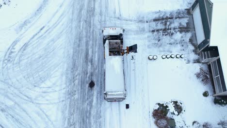 Top-down-drone-shot-of-a-city-dump-truck-picking-up-trash-with-snow-covered-roads