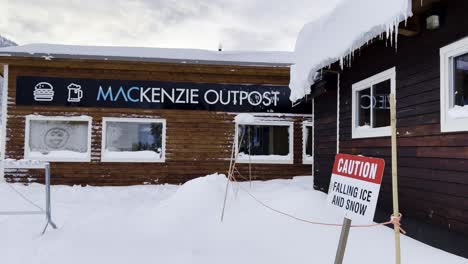 Mt-MacKenzie-Outpost-with-falling-snow-hanging-icicles-and-caution-falling-snow-sign-in-foreground-at-Revelstoke-British-Columbia-Canada