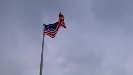 The-flag-of-America-flutters-in-the-wind,-with-gray-clouds-in-the-background