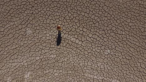 Wide-aerial-view-of-a-girl-walking-alone-across-a-dry,-barren-landscape-during-a-drought-in-Cyprus,-Greece