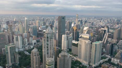 Luftbild-Durch-Skyline-Und-Wolkenkratzer-Des-Bezirks-Sukhumvit,-Pathum-Wan-Und-Lumphini-Park-Während-Des-Sonnenuntergangs-In-Bangkok,-Thailand