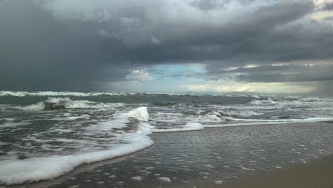 Meereswellen-Laufen-über-Das-Sandige-Ufer,-Gewitterwolken-Im-Hintergrund