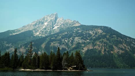 Stunning-landscape-nature-tilting-up-shot-of-the-majestic-Grand-Teton-National-Park-mountain's-from-Jenny-Lake-on-a-warm-sunny-summer-day-near-Jackson-Hole,-Wyoming,-USA