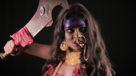 Live-Indian-Goddess-Kali-looks-at-camera-with-sword,-Indian-goddess-cosplay-with-long-hair-and-dark-background