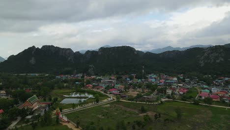 Descending-aerial-footage-of-this-lovely-fishing-village,-Buddhist-temple,-mountains-and-sky