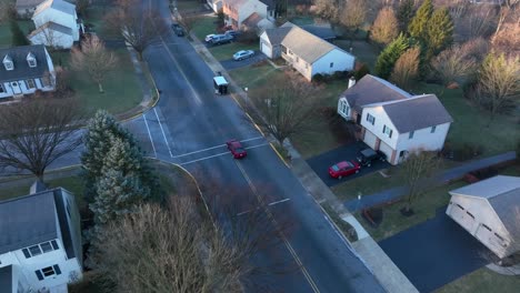 Aerial-tracking-shot-of-red-car-driving-through-American-suburb-in-winter