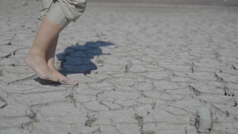 Bare-feet-walking-slowly-across-dry-and-cracked-dirt,-during-a-drought