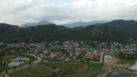 Aerial-footage-sliding-towards-the-right-revealing-a-Buddhist-temple,-fishing-village,-gorgeous-mountains-and-sky