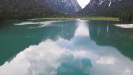 Drone-Volando-De-Un-Turista-En-Un-Bote-Pequeño-En-Medio-Del-Hermoso-Lago-Glacial-Reflectante-Rodeado-De-árboles-En-Los-Dolomitas-En-Italia