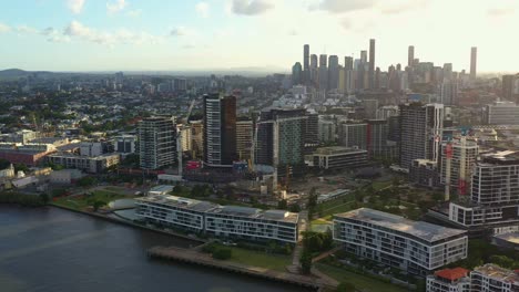 Aerial-drone-fly-around-Newstead-river-terrace,-waterfront-residential-apartment-complex-along-Brisbane-river-with-downtown-cityscape-on-the-skyline-at-sunset-golden-hour,-capital-city-of-Queensland