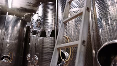 Shiny-stainless-steel-tanks-in-wine-cellar-used-for-wine-fermentation,-tilt-up