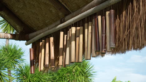 Bamboo-wind-chimes-hang-from-thatched-roof-of-outdoor-shed-with-wooden-poles