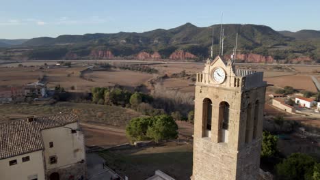Panorámica-Sobre-La-Torre-De-Una-Iglesia-Con-La-Entrada-Del-Sol-Y-Un-Paisaje-De-Fondo