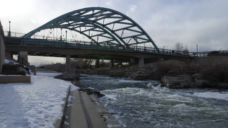 Speer-Boulevard-Bridge-Over-South-Platte-River-In-Denver,-Colorado-With-Snowy-Riverbank-In-Winter