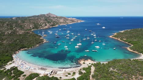 Boats-and-yachts-floating-in-turquoise-blue-cove-at-La-Maddalena-Island,-Sardinia---Aerial-4k-Circling