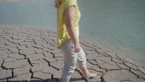 Medium-shot-of-a-girl-approaching-water-after-walking-across-a-dry,-cracked-desert-landscape
