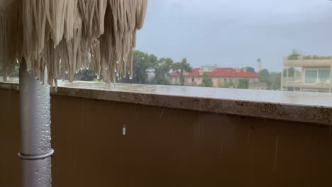 Regentropfen-Fallen-Auf-Die-Brüstung-Und-Den-Zusammengeklappten-Sonnenschirm-Auf-Dem-Balkon