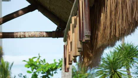 Row-of-Bamboo-wind-chimes-hang-on-wooden-poles-from-thatched-roof-of-outdoor-Gazebo