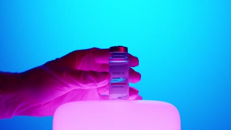 hand-with-latex-gloves-place-Covid-19-vaccine-vial-on-bright-LED-lamp