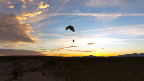 Silhouette-of-a-powered-paraglider-flying-over-the-Mojave-Desert-during-a-colorful-sunset