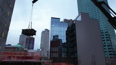 Boom-crane-lifting-material-to-a-urban-construction-in-middle-of-high-rise-in-NY---Aerial-view